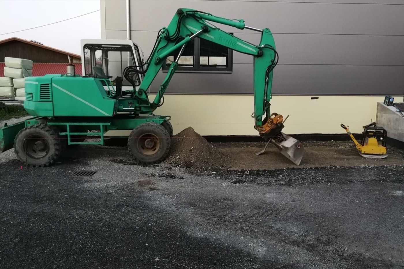 Mobilbagger arbeitet dicht an der Hauswand, daneben eine frisch geschotterte Fläche
