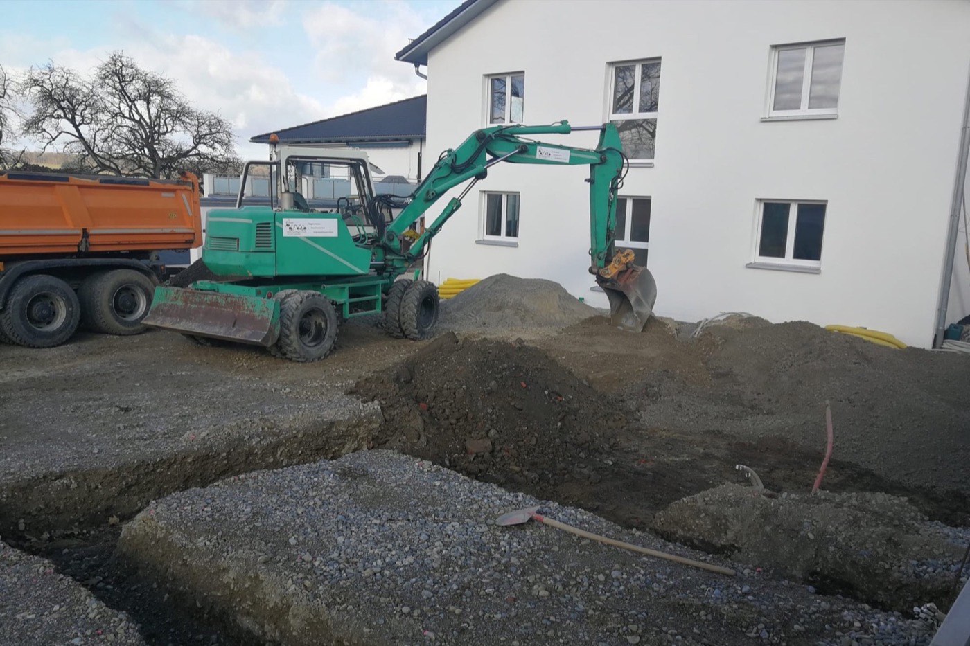 Mobilbagger vor einem Neubau, davor Kies- und Erdhaufen