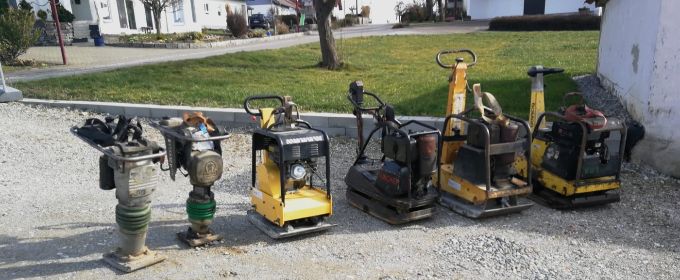 Zwei Vibrationsstampfer und vier Rüttelplatten aufgereiht auf einem Kiesplatz
