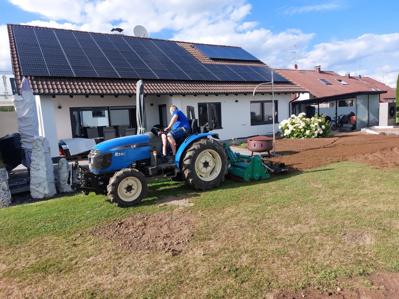 Traktor mit angebauter Bodenfräse arbeitet eine Gartenfläche für neuen Rasen um